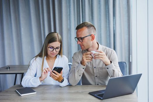 Young business team, male and female colleagues talking at work, discussing a new project with a laptop, young executives having a friendly conversation, collaborating in teamwork in the office