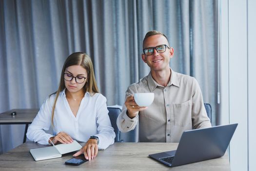 Young business team, male and female colleagues talking at work, discussing a new project with a laptop, young executives having a friendly conversation, collaborating in teamwork in the office