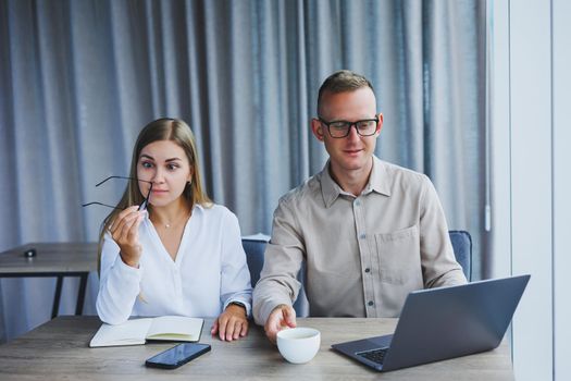 Young business team, male and female colleagues talking at work, discussing a new project with a laptop, young executives having a friendly conversation, collaborating in teamwork in the office