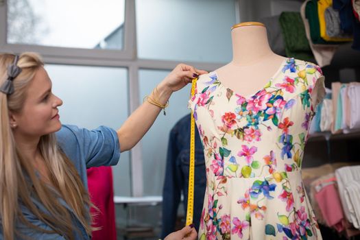 A clothing designer measures a freshly sewn dress, which is put on a mannequin. Tailor's workshop at work.