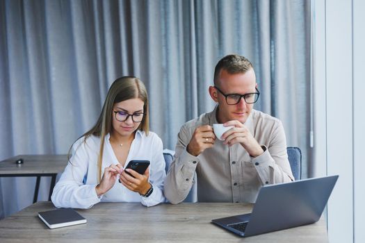 Young business team, male and female colleagues talking at work, discussing a new project with a laptop, young executives having a friendly conversation, collaborating in teamwork in the office