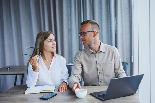 Young business team, male and female colleagues talking at work, discussing a new project with a laptop, young executives having a friendly conversation, collaborating in teamwork in the office