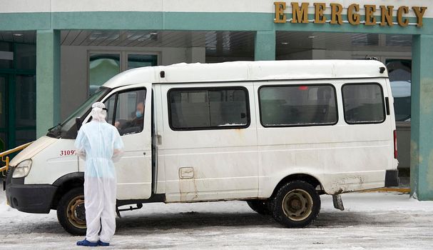 People in protective suits helping a sick person outdoors, coronavirus concept. Ambulance car.