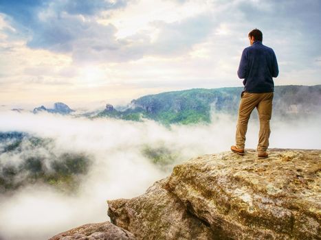 Photographer bend head check display of camera. Man stay on cliff and takes photos. Autumn beautiful misty landscape misty sunrise at horizon