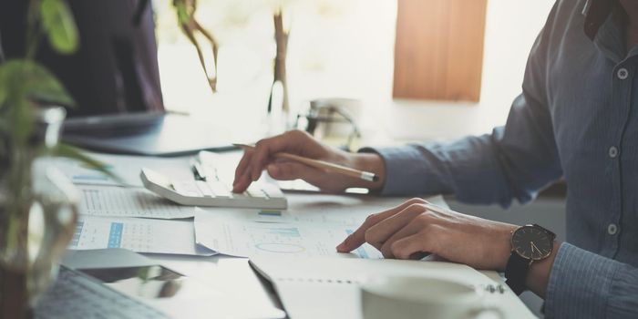 Close up Business woman using calculator and laptop for do math finance on wooden desk in office and business working background, tax, accounting, statistics and analytic research concept.