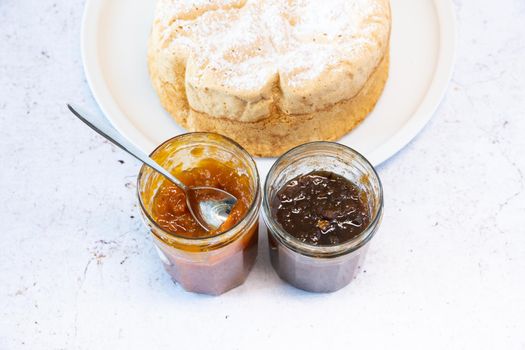 Homemade Savoie cake on a pretty white porcelain dish with jam in a jar