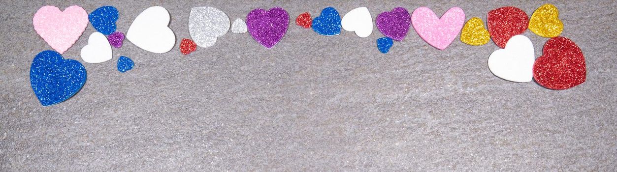 colorful hearts of glitter of all colors on a gray granite background. Concept of valentines day and love in general.