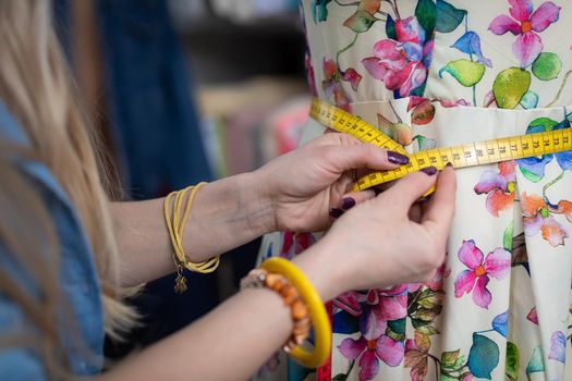 The designer checks the waist circumference with a tailor's centimeter. The tailor works during working hours.