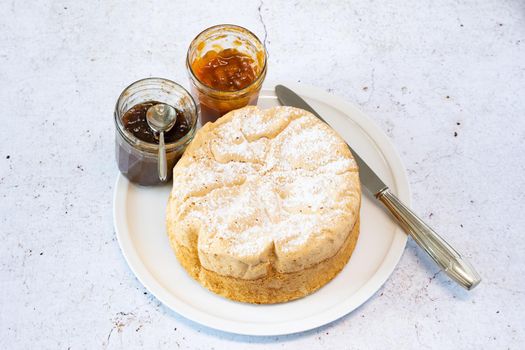 Homemade Savoie cake on a pretty white porcelain dish with jam in a jar