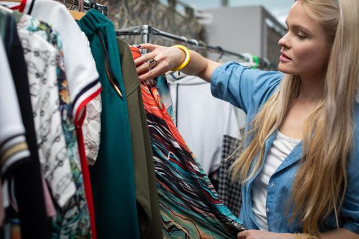 A woman looks at the new clothes hanging on the hangers. A blonde woman with long hair looks for the right blouse for her.