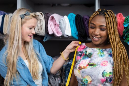 A clothing designer measures a dark-skinned girl who wants to sew her next dress. Many braided hair braids on her head.