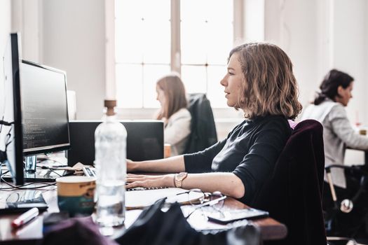Women in startup business and entrepreneurship. Yound devoted female AI programmers and IT software developers team programming on desktop computer in startup company share office space.