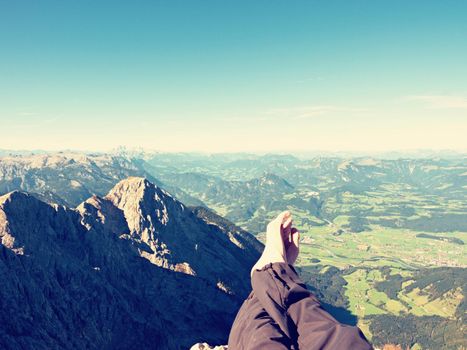 The crossed legs take a  rest on tiring mountain trail. Sweaty male legs in dark trekking trousers relaxing on peak of mountain above valley. 