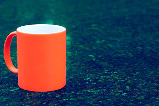 a small bowl-shaped container for drinking from, typically having a handle. Red ceramic cup mug on dark green emerald spotted background