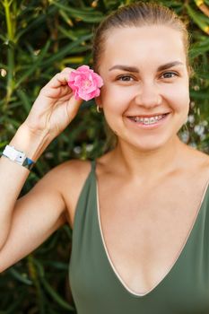 Portrait of a pretty blonde woman in a top and denim shorts, summer vacation, a girl with a pink flower near her face