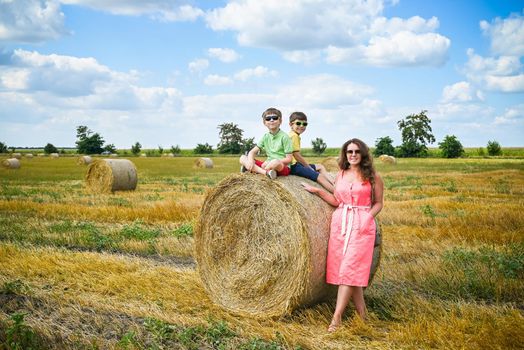 Happy family in a wheat field. Mother and two sibling brother boy on a Round Bales at summer time.