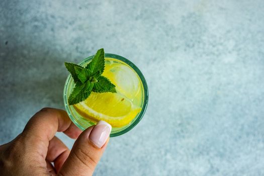 Mojito cocktail with mint and lemon served in the crystal glass in woman hands