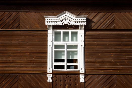 Old wooden house with a white window in Russian style. Wooden window with white trim. Russian village, old window, copy space. Simple rustic style. Sunny bright day in summer.