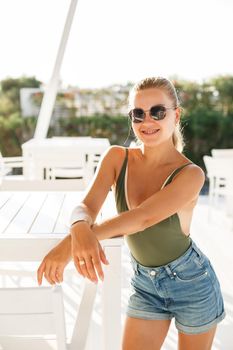 Blond woman beautiful face tanned skin dressed in green top and denim shorts fashion clothing style summer clothes collection, summer and leisure