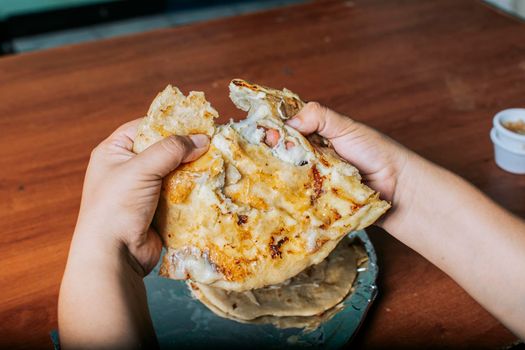 View of hands dividing delicious Salvadoran pupusas on wooden table. Concept of traditional handmade pupusas, Hands dividing delicious Nicaraguan pupusa on the table