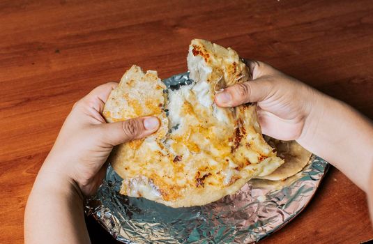 Hands dividing delicious Nicaraguan pupusa on the table, View of hands dividing delicious Salvadoran pupusas on wooden table. Concept of traditional handmade pupusas