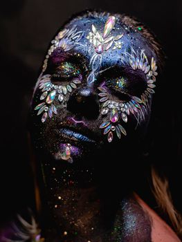 Creative makeup girl with rhinestones and feathers on a dark background