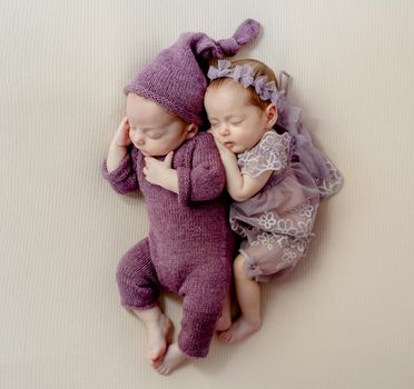 Newborn babies twins wearing beautiful costumes lying together and sleeping. Cute infant child kids brother and sister napping and hugging each other studio photoshoot