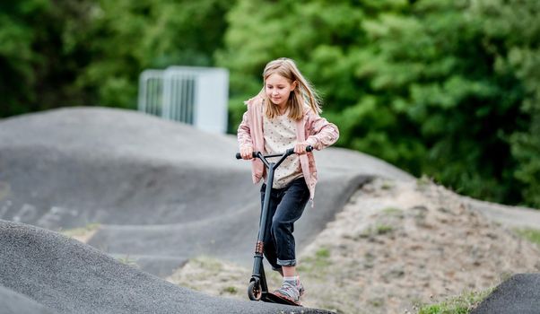 Preteen girl riding scooter in city park at spring time. Pretty child kid having fun with vehicle outdoors