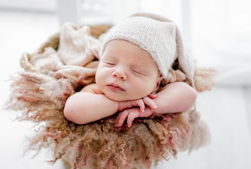 Newborn baby child wearing hat sleeping and holding hands under cheeks. Sweet infant kid napping closeup portrait