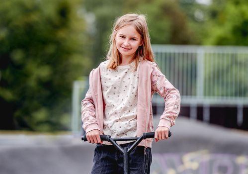 Preteen girl with scooter in city park at spring time portrait. Pretty child kid model posing with vehicle