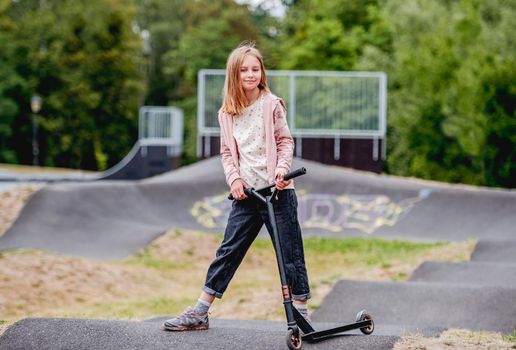 Preteen girl with scooter in city park at spring time. Pretty child kid model posing with vehicle