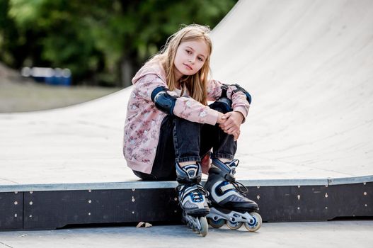 Cute girl roller skater sitting in city park and looking at camera Pretty female preteen kid child posing during rollerskating