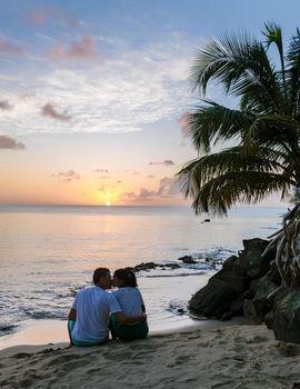 couple watching the sunset at the ocean on a tropical beach in Saint Lucia, St. Lucia Caribbean Sea. Asian women and caucasian men watching sunset by a palm tree