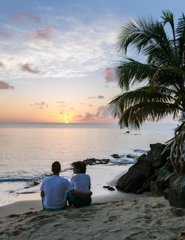 couple watching the sunset at the ocean on a tropical beach in Saint Lucia, St. Lucia Caribbean Sea. Asian women and caucasian men watching sunset by a palm tree
