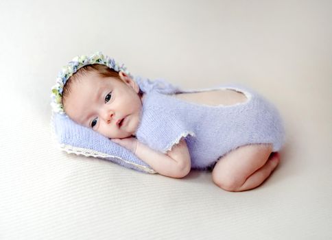 Newborn baby girl wearing knitted costume and wreath lying on pillow. Cute infant child kid istudio photoshoot