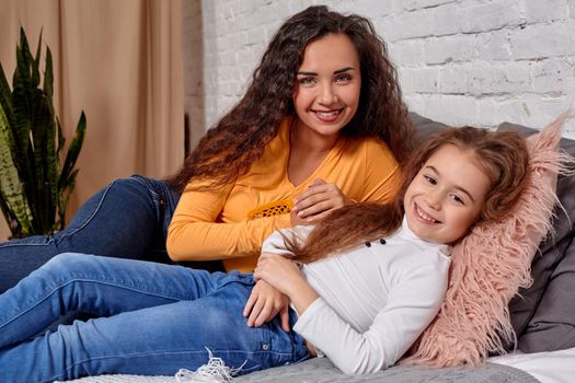 Love of young mother and daughter. They lie on the bed at home and have fun, they feel good.