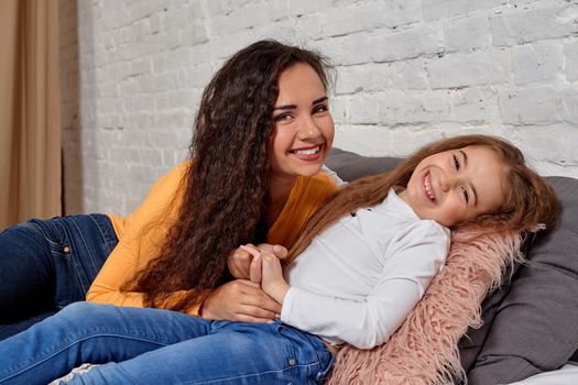 Love of young mother and daughter. They lie on the bed at home and have fun, they feel good.