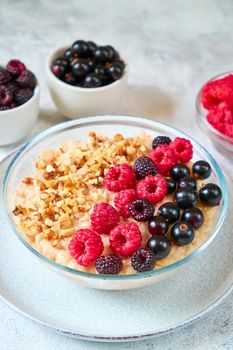 Oatmeal with raspberries, blackcurrants and crushed nuts in a glass bowl. Healthy balanced food.