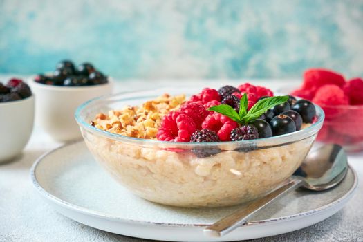 Close-up oatmeal with different berries and crushed nuts in a glass bowl. Healthy balanced food.
