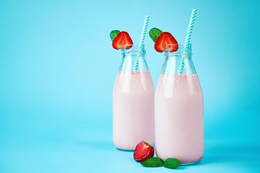 Close-up strawberry smoothie or milkshake in glass jar with berries on blue background. Healthy summer drink.