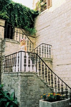Bride in a wreath stands on the stone steps of the building holding the handrail. High quality photo