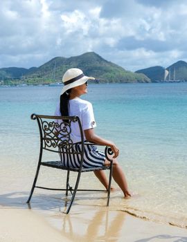 young women on a chair with their feet in the ocean watching the beautiful Caribbean ocean of St Lucia. Asian women with hat looking at the ocean