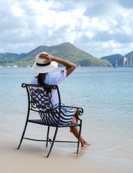 young women on a chair with their feet in the ocean watching the beautiful Caribbean ocean of St Lucia. Asian women with hat looking at the ocean