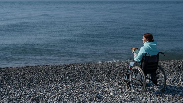 Caucasian woman in a wheelchair cuddling with a dog near the sea