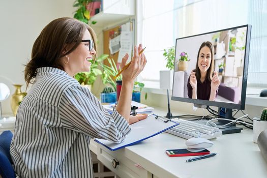 Mature woman talking online with young female using video call on computer, home interior. Virtual meeting, therapy session with psychologist. Chat conference technology psychology education business