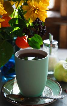 Green cup of tea on green plate with a bouquet of yellow autumn flowers, early autumn morning concept, selective focus.