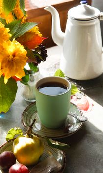 Green cup of tea on green plate, white teapot and a bouquet of autumn yellow flowers, early autumn morning concept.