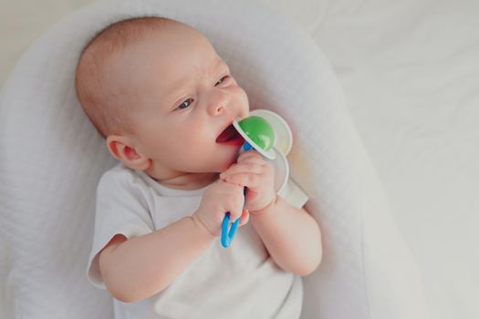 The kid is gnawing on a lifestyle rattle . Children's toys. An article about children. An article about children's toys. An article about teething. The rattle is colored. Copy Space