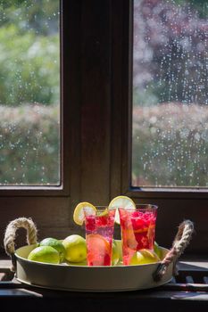 Refreshing raspberry and lime lemonade in pink glasses on the windowsill in the bright rays of the sun, high quality photo
