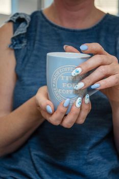 a young woman holds a blue cup of coffee, a beautiful summer manicure. High quality photo